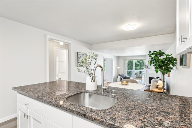kitchen with white cabinets, dark stone countertops, a sink, a fireplace, and open floor plan