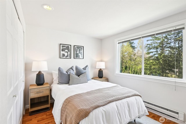 bedroom with a baseboard heating unit, wood finished floors, and recessed lighting
