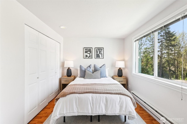 bedroom featuring baseboard heating, wood finished floors, a closet, and multiple windows