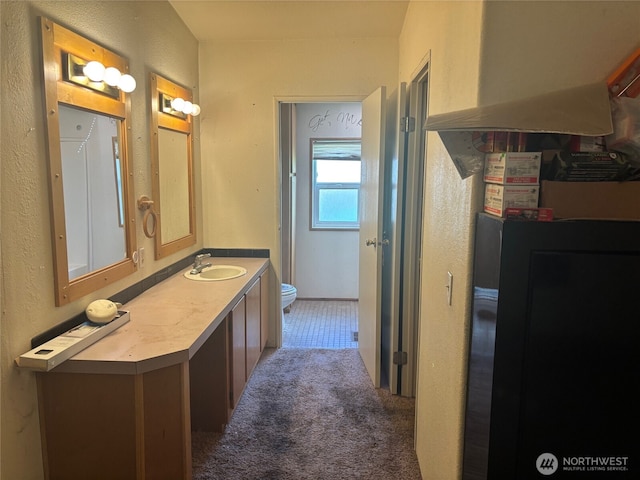 bathroom with a textured wall, toilet, and vanity