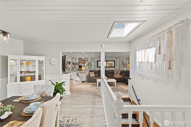 dining area with a skylight, light wood-style floors, and wainscoting