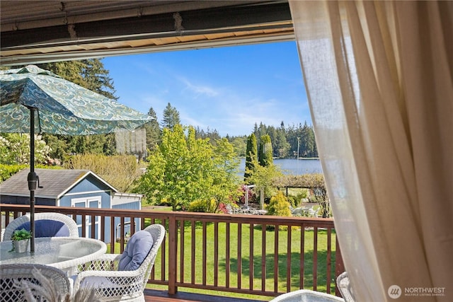 wooden terrace featuring outdoor dining area, a storage unit, a yard, an outbuilding, and a water view