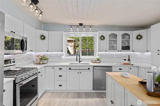 kitchen featuring appliances with stainless steel finishes, a sink, healthy amount of natural light, wooden ceiling, and white cabinets