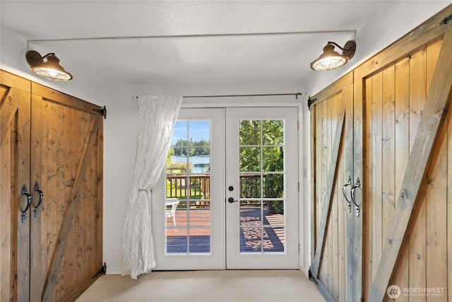 entryway with french doors, light colored carpet, a water view, and wooden walls