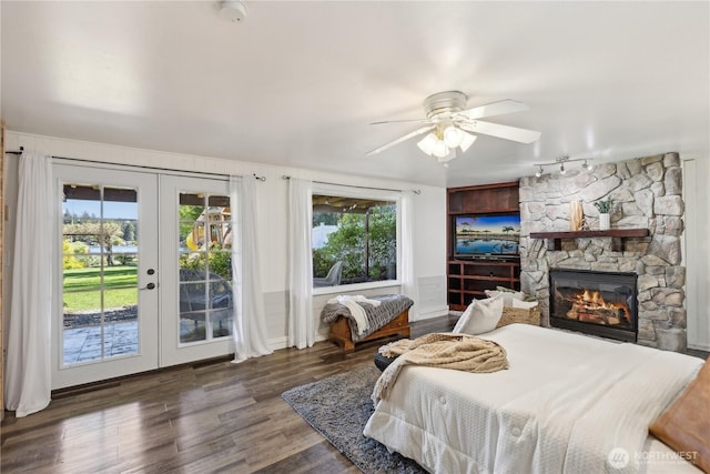 bedroom with access to outside, french doors, wood finished floors, a stone fireplace, and rail lighting