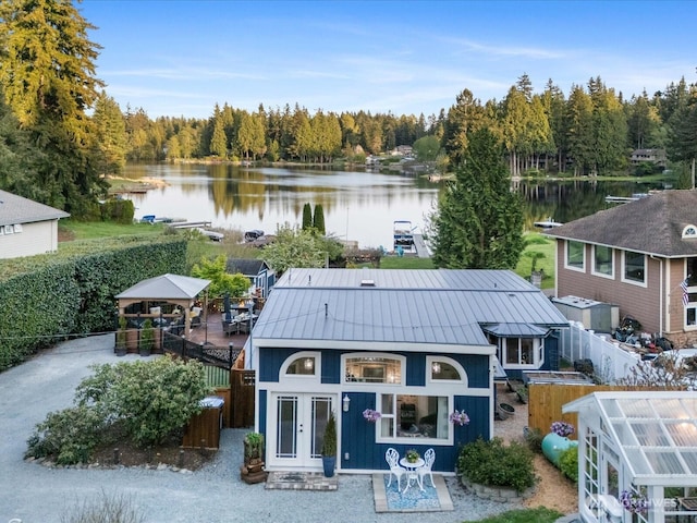 exterior space featuring a water view, a standing seam roof, metal roof, a view of trees, and fence