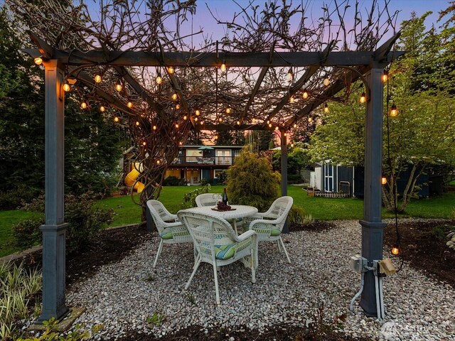 patio terrace at dusk featuring a pergola, a yard, and outdoor dining space
