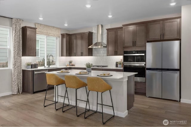 kitchen featuring a sink, stainless steel appliances, decorative backsplash, a center island, and wall chimney exhaust hood