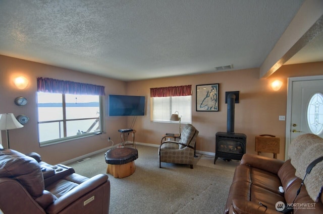 carpeted living room featuring visible vents, a wood stove, baseboards, and a textured ceiling