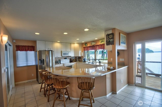 kitchen with light tile patterned floors, white appliances, a peninsula, a sink, and baseboards