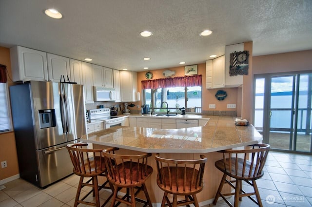 kitchen with tile counters, white appliances, a peninsula, white cabinetry, and light tile patterned flooring