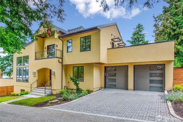 townhome / multi-family property featuring a balcony, stucco siding, decorative driveway, a garage, and fence