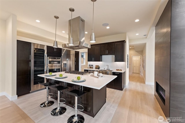 kitchen with a center island, light countertops, a breakfast bar area, appliances with stainless steel finishes, and island range hood