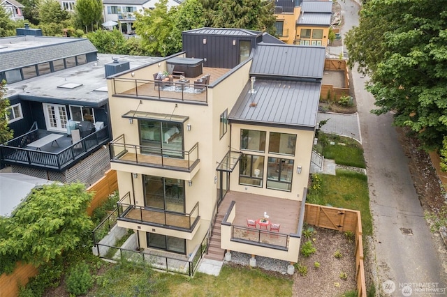rear view of property featuring a standing seam roof, stucco siding, fence private yard, metal roof, and a balcony