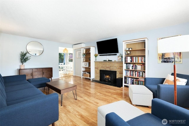 living area with a wall mounted AC, light wood finished floors, and a fireplace