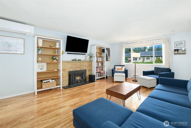 living room featuring baseboard heating, an AC wall unit, light wood-type flooring, and a brick fireplace