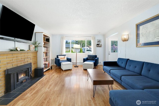 living area featuring a baseboard radiator, a fireplace, a textured ceiling, and wood finished floors