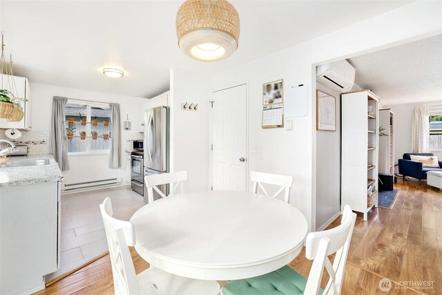 dining space with light wood-type flooring, a baseboard radiator, and a wall mounted air conditioner
