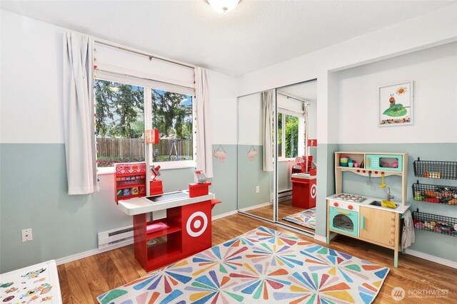 playroom with baseboards, a baseboard heating unit, and wood finished floors