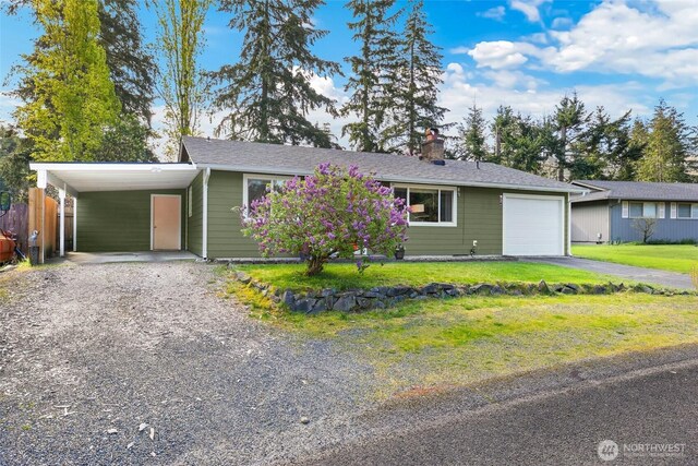 ranch-style home featuring an attached garage, aphalt driveway, a front yard, a chimney, and a carport