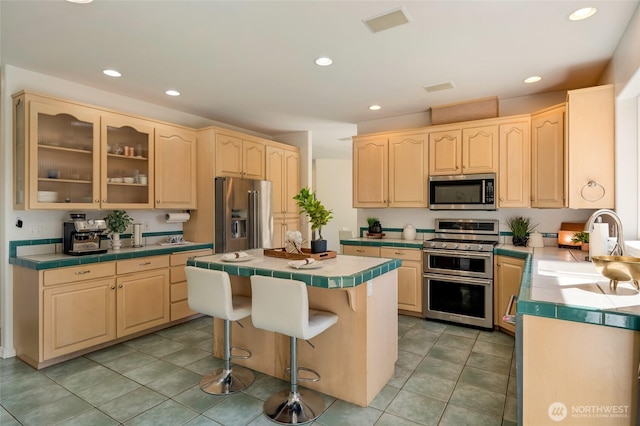 kitchen with light brown cabinets, a sink, tile counters, and stainless steel appliances