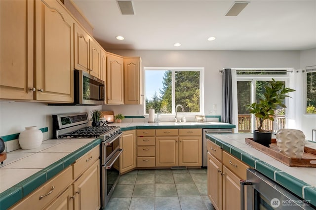 kitchen with tile counters, plenty of natural light, light brown cabinetry, and appliances with stainless steel finishes