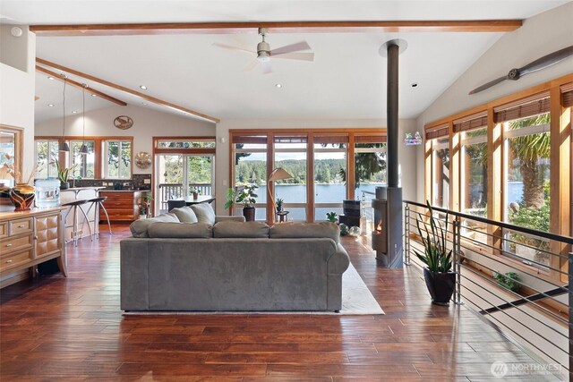 14407 Goodrich Dr NW, Gig Harbor, WA 98329 - living room featuring dark wood-style floors, a ceiling fan, a wood stove, a water view, and vaulted ceiling with beams