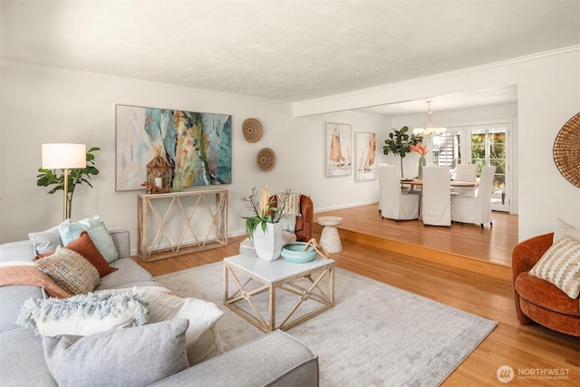 living room featuring a notable chandelier, baseboards, ornamental molding, and wood finished floors