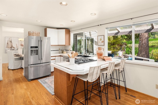 kitchen featuring stainless steel fridge with ice dispenser, a breakfast bar, visible vents, and a wealth of natural light