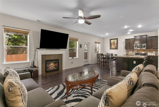 living room with a ceiling fan, a tiled fireplace, dark wood finished floors, visible vents, and recessed lighting