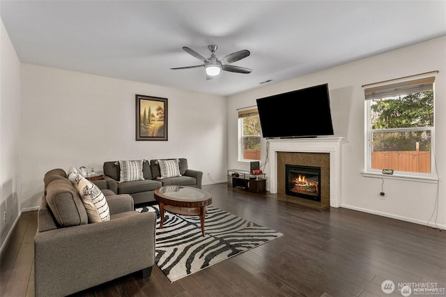 living area with visible vents, baseboards, a glass covered fireplace, wood finished floors, and ceiling fan