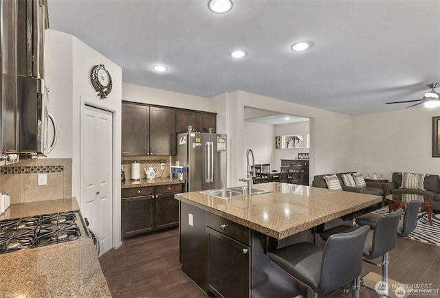 kitchen featuring a sink, dark brown cabinets, open floor plan, a breakfast bar, and appliances with stainless steel finishes