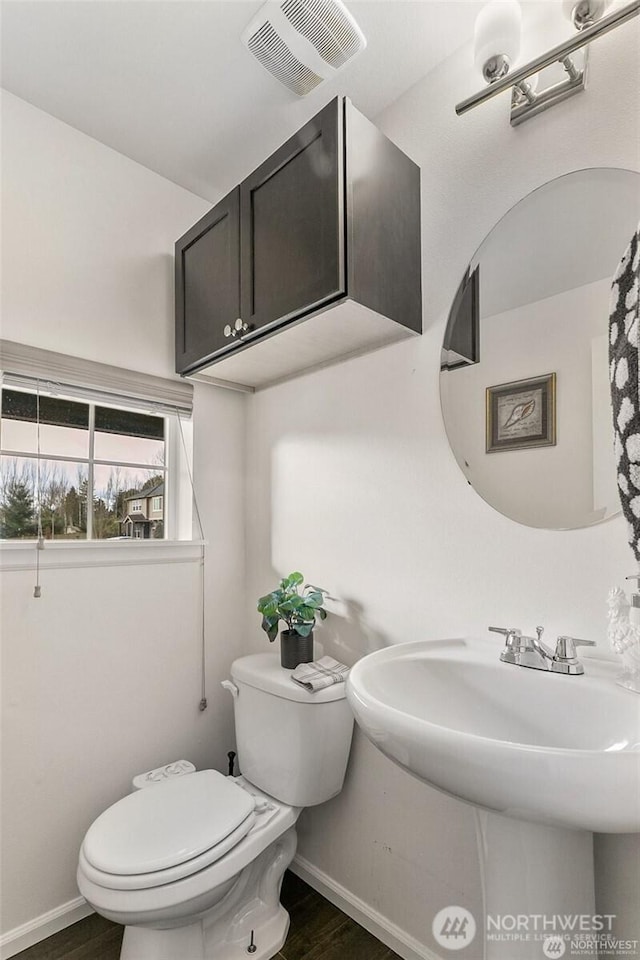 half bathroom with a sink, toilet, baseboards, visible vents, and wood finished floors