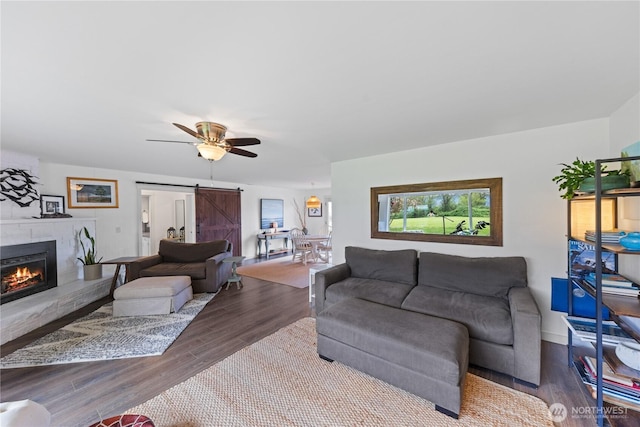 living area with a barn door, a ceiling fan, a warm lit fireplace, and wood finished floors