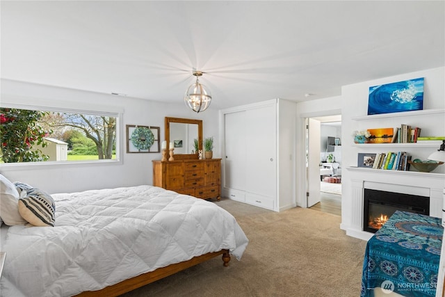 bedroom featuring an inviting chandelier, carpet, and a glass covered fireplace