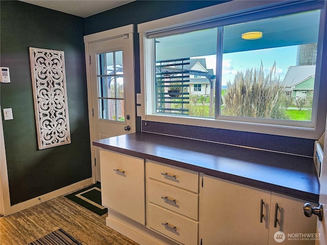 interior space with white cabinetry, dark countertops, dark wood-style floors, and baseboards