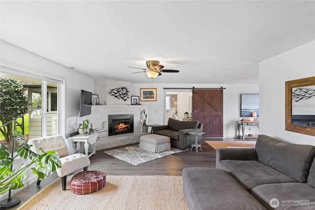 living area with dark wood-style flooring, a large fireplace, a ceiling fan, and a barn door
