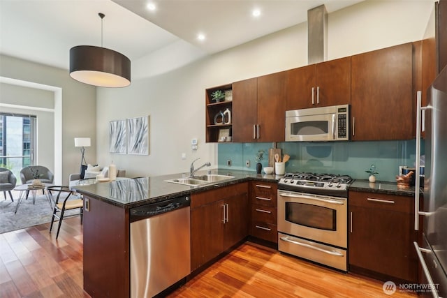 kitchen with open shelves, a peninsula, a sink, light wood finished floors, and stainless steel appliances