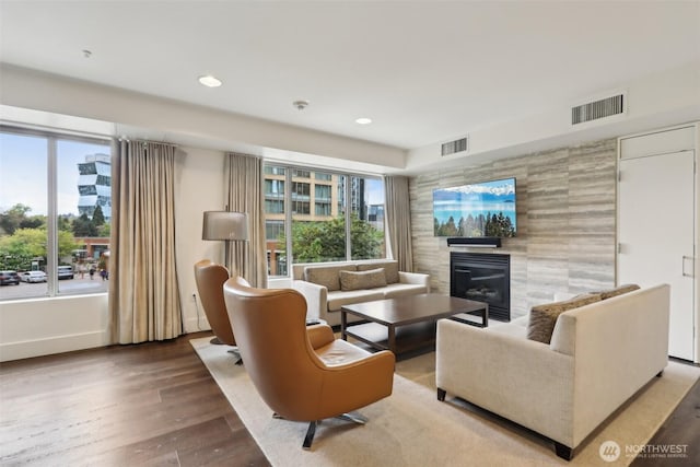 living area with visible vents, plenty of natural light, wood finished floors, and a tile fireplace