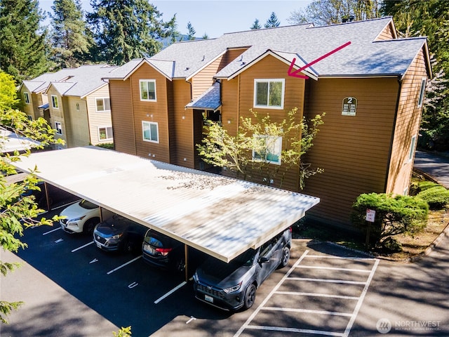rear view of property featuring covered and uncovered parking and a shingled roof