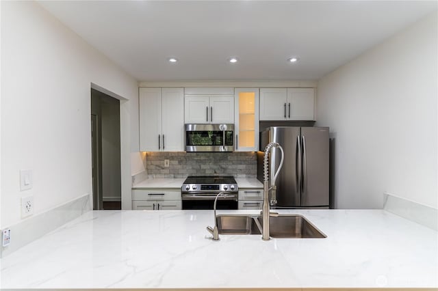 kitchen featuring recessed lighting, light stone countertops, a sink, stainless steel appliances, and glass insert cabinets