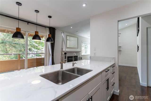 kitchen with a premium fireplace, a sink, dark wood-style flooring, decorative light fixtures, and light stone counters