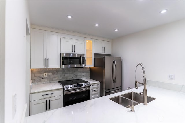 kitchen featuring tasteful backsplash, glass insert cabinets, a sink, stainless steel appliances, and light stone countertops