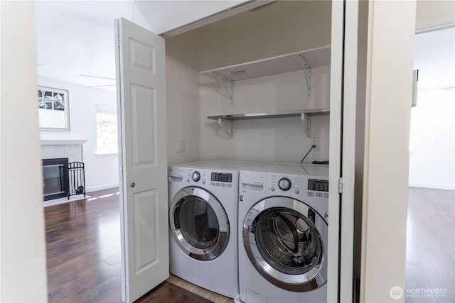 clothes washing area featuring separate washer and dryer, laundry area, a glass covered fireplace, dark wood-type flooring, and baseboards