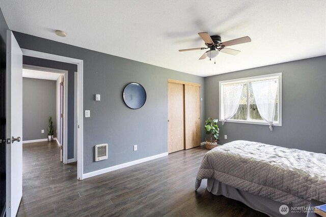 bedroom featuring ceiling fan, dark wood finished floors, a closet, baseboards, and heating unit