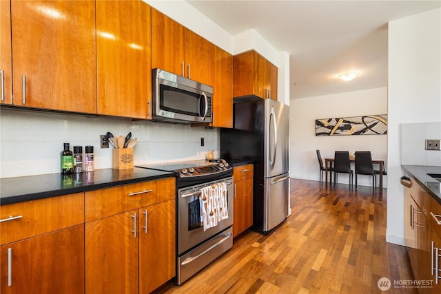 3104 Western Ave Unit 603, Seattle, WA 98121 - kitchen featuring backsplash, dark countertops, dark wood-type flooring, brown cabinets, and appliances with stainless steel finishes