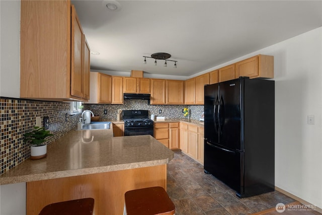kitchen with decorative backsplash, a sink, light countertops, black appliances, and under cabinet range hood