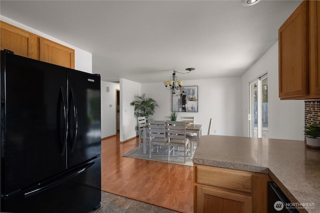 kitchen featuring dark countertops, an inviting chandelier, brown cabinetry, freestanding refrigerator, and a peninsula