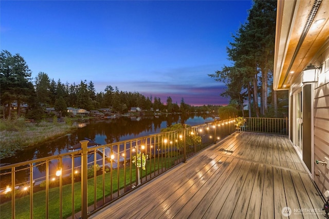 deck at dusk featuring a lawn and a water view