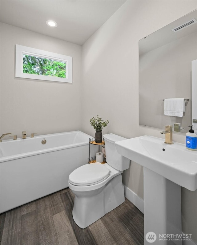 full bath featuring toilet, a freestanding bath, wood finished floors, baseboards, and recessed lighting